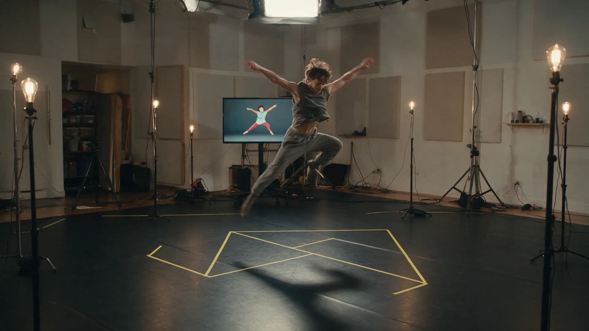 A performer mid-leap mirrored as an animated figure on a studio monitor