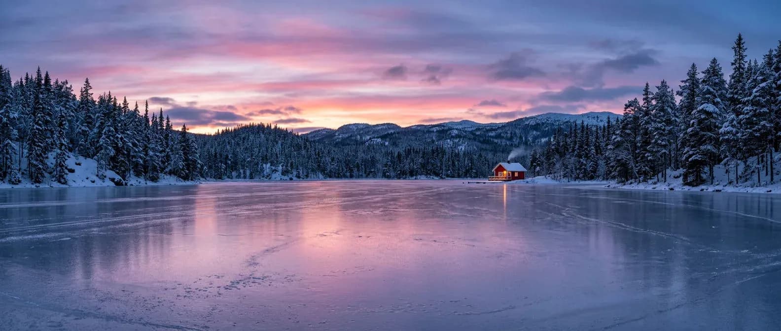 Ultra-wide panorama of a frozen lake between snowy pines at blue hour with a red cabin on the far shore