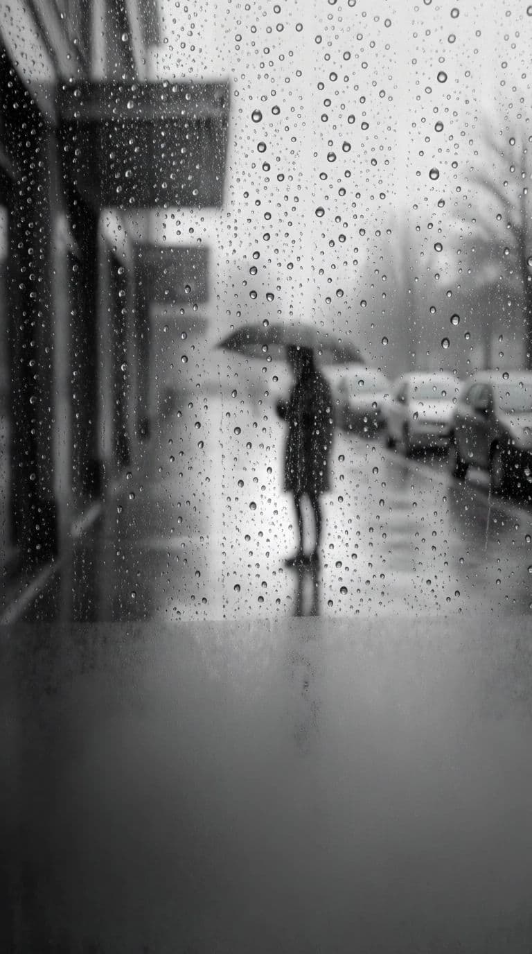 Black and white photograph of rain on a window with a blurred figure beyond, generated with Krea 2 Medium