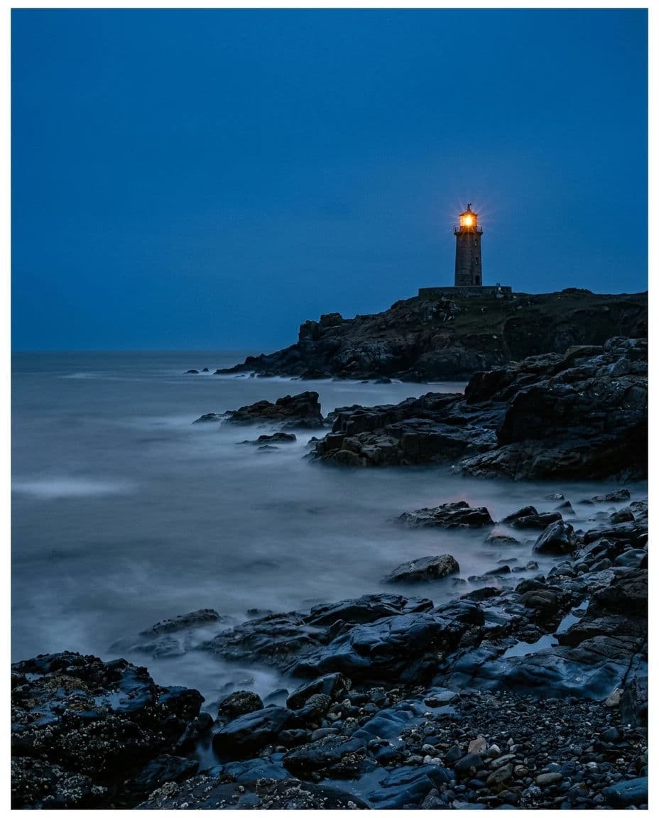 Coastal photograph at blue hour with a lighthouse lamp lit against a deep blue sky, generated with Nano Banana 2