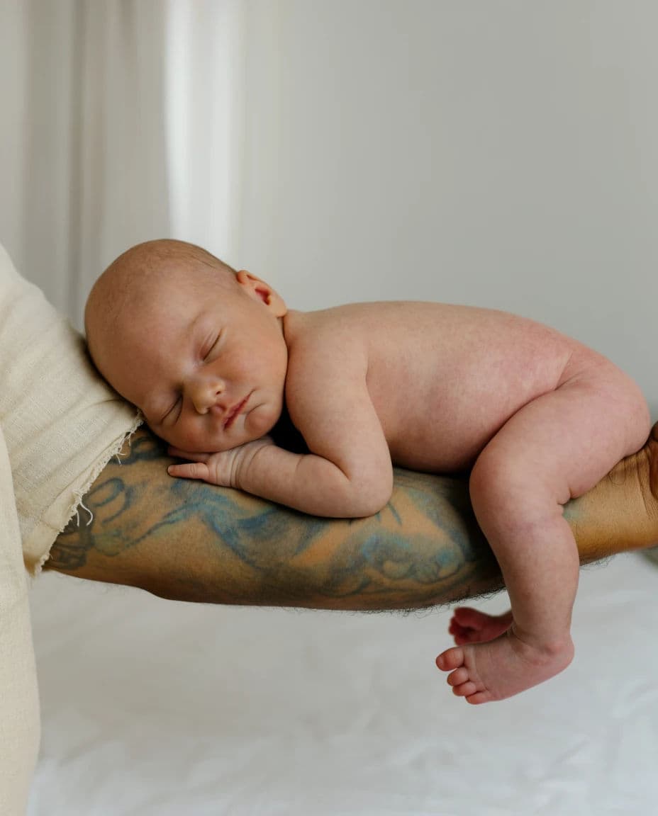 Close portrait of a newborn asleep along a father tattooed forearm in soft indirect light, generated with Krea 2 Large