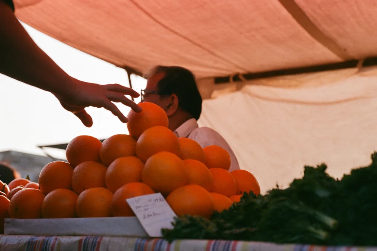 Street photograph of a hand reaching into a pyramid of oranges at a market stall, generated with Krea 2 Medium